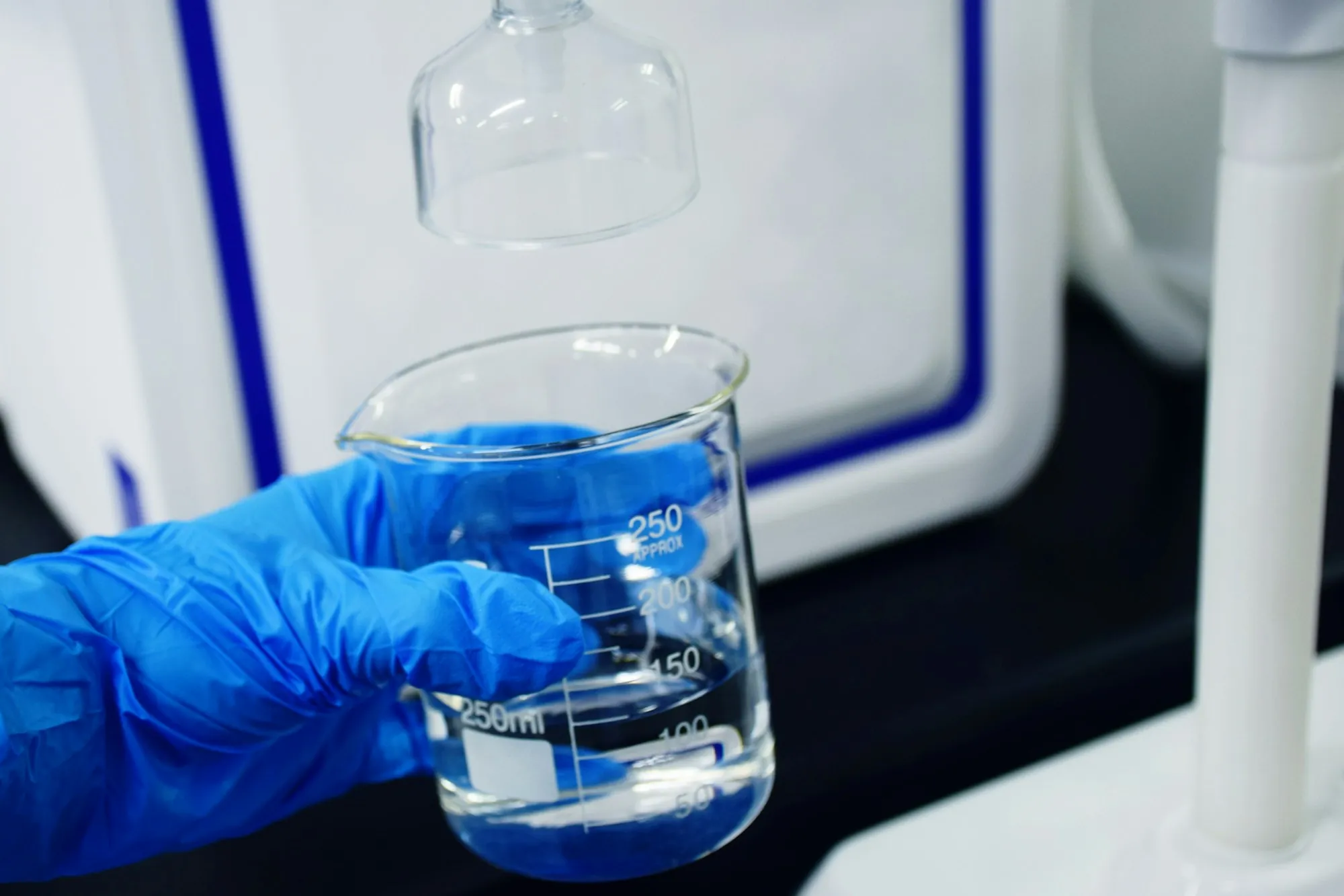 Gloved hand holding a beaker of water beside lab equipment