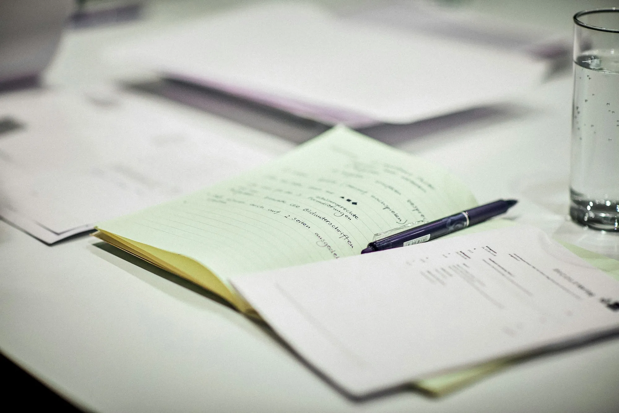 Notebook and paperwork on a desk beside a glass of water