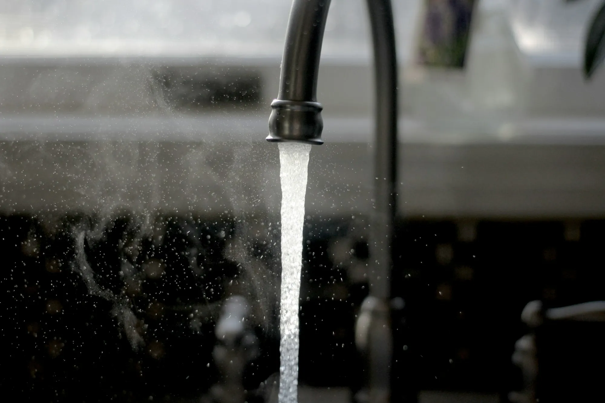 Water running from a kitchen faucet against a dark background