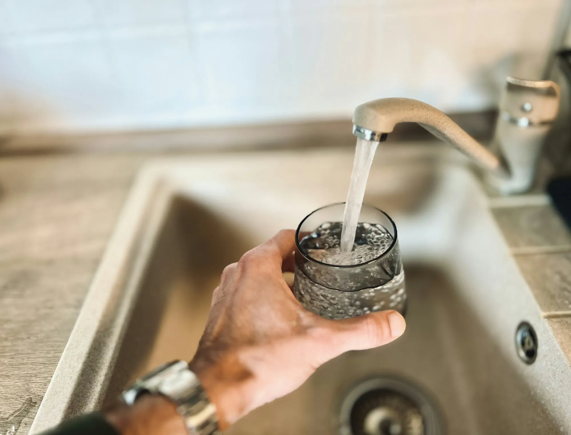 Hand filling a glass with tap water at a kitchen sink
